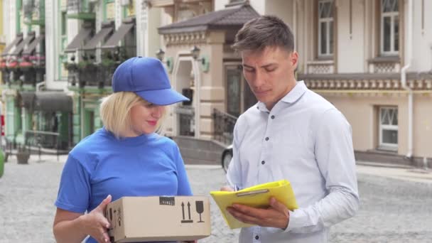 Bello giovane uomo che firma i documenti che riceve un pacco dalla donna di consegna — Video Stock