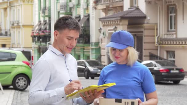 Mensajera entregando un paquete a un joven en la calle de la ciudad — Vídeos de Stock