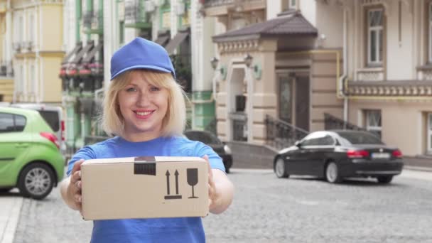 Cheerful delivery woman in blue uniform holding cardboard box — Stock Video