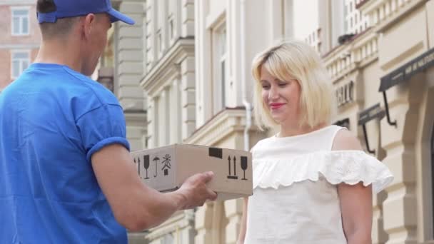 Lovely woman receiving cardboard box parcel from a delivery man — Stock Video
