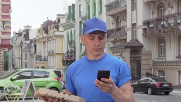 Mensageiro masculino entregando pizza na cidade chamando é cliente no telefone — Vídeo de Stock