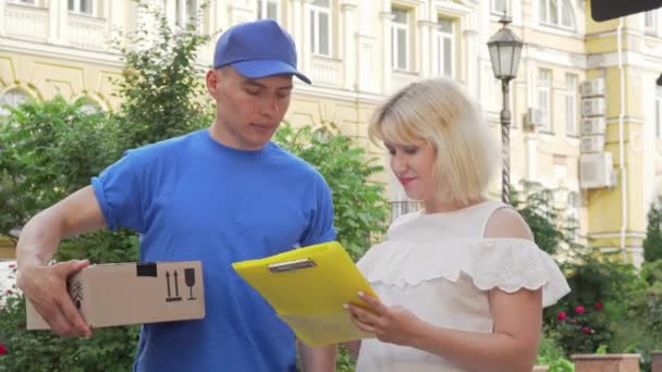 Glückliche Frau unterschreibt Quittung und erhält ein Paket vom Kurier — Stockvideo