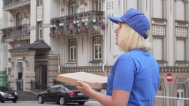 Pizza kutusunu tutan sokakta etrafa bakan bir teslimatçı kadının arka görüş fotoğrafı