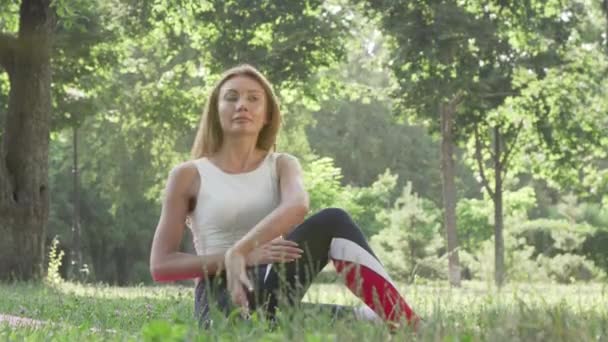 Härlig kvinna som tränar yoga på gräset i parken — Stockvideo