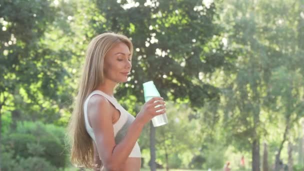 Schöne, fröhliche Frau lächelt in die Kamera, nachdem sie Wasser getrunken hat — Stockvideo