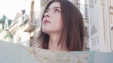 Şehirde bir harita kullanarak etrafa bakan güzel bir kadının kırpılmış çekim