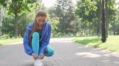 Güzel sporcu parkta koşmadan önce ayakkabı bağcıklarını bağlayarak