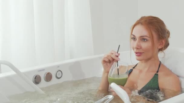 Sliding shot of a beautiful woman sipping delicious smoothie in whirl pool bath — Stock Video