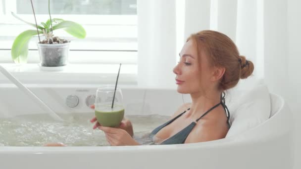 Encantadora mujer bebiendo batido de desintoxicación sentada en el baño de hidromasaje de la piscina — Vídeos de Stock