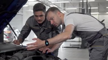 Oto tamircileri, garajlarında kaputun altına bakan bozuk arabayı tartışıyor