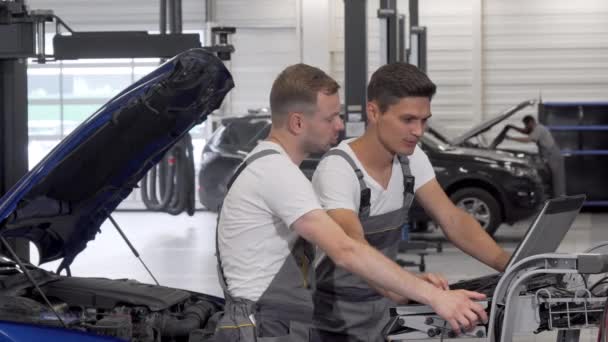 Twee monteurs doen computer diagnostiek van een gebroken auto — Stockvideo