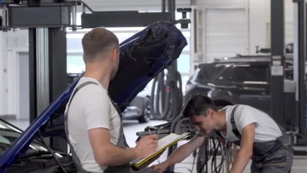 Dois mecânicos discutem a reparação de automóveis quebrados na garagem — Vídeo de Stock