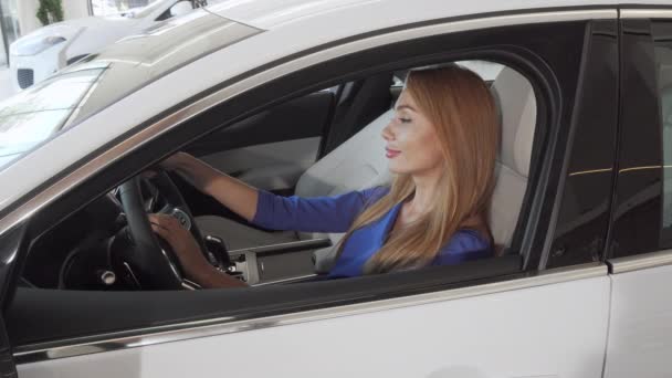 Schöne Fahrerin lächelt in die Kamera, sitzt in einem neuen Auto im Autohaus — Stockvideo