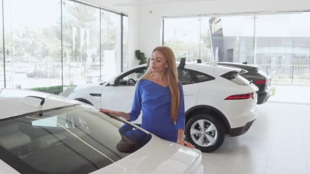 Hermosa mujer examinando el coche caro en el concesionario — Vídeo de stock