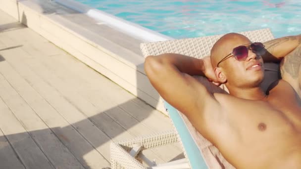 Corredera de un hombre africano guapo tomando el sol junto a la piscina — Vídeos de Stock