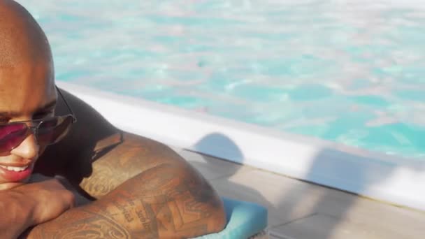 Tiro deslizante de um homem africano feliz desfrutando de banhos de sol na piscina — Vídeo de Stock