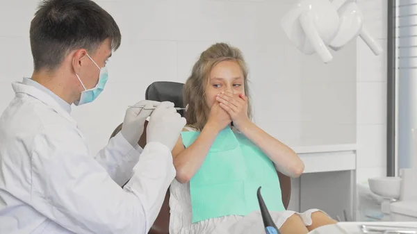 Giovane ragazza che rifiuta di mostrare i denti a un dentista che si copre la bocca con le mani — Foto Stock