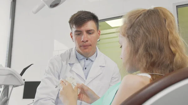 Profesyonel diş hekimi diş bakımı açıklayan genç hasta ile konuşuyor — Stok fotoğraf
