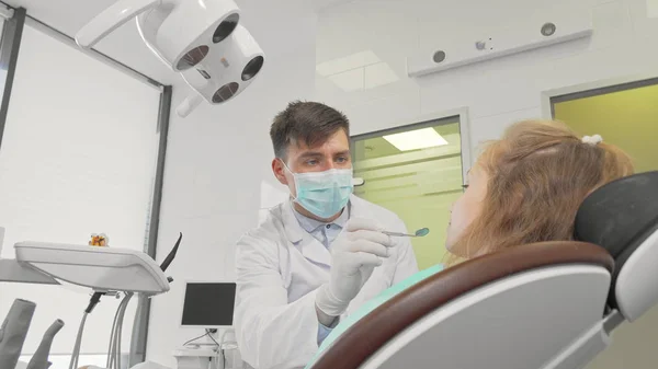 Homem dentista trabalhando em sua clínica verificando dentes de uma menina — Fotografia de Stock