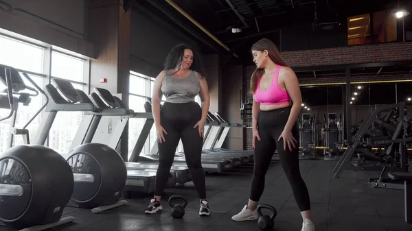 Spor salonunda kettlebells ile çömelme iki güzel artı boyutu kadın sporcular — Stok fotoğraf