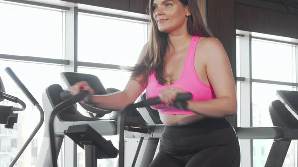 Beautiful curvy woman smiling to the camera doing cardio on air bike at gym