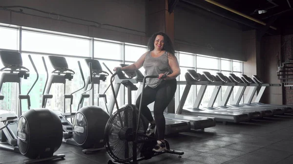 Spor salonunda hava bisikleti üzerinde çalışan mutlu artı boyutu kadın tam uzunlukta çekim — Stok fotoğraf