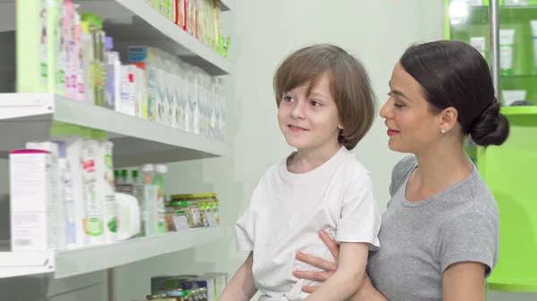 Schöne Frau und ihr kleiner Sohn begutachten Produkte, die in der Apotheke verkauft werden — Stockfoto