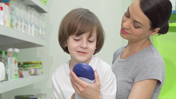 Beautiful woman choosing shower gel for her adorable son at drugstore — Stock Photo, Image