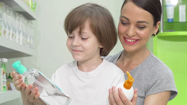Vacker kvinna och hennes son välja mellan två produkter på apotek — Stockfoto