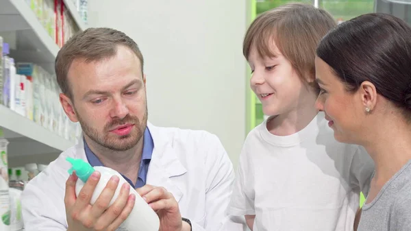 Farmacêutico masculino alegre ajudando jovem mulher com filho pequeno — Fotografia de Stock