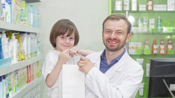 Farmacêutico alegre sorrindo para a câmera com um menino bonito — Fotografia de Stock