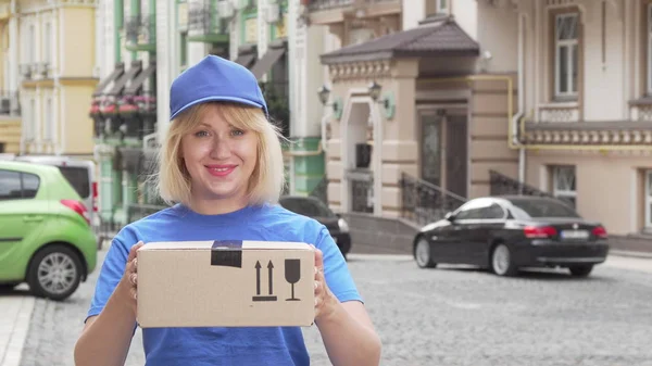Cheerful delivery woman in blue uniform holding cardboard box