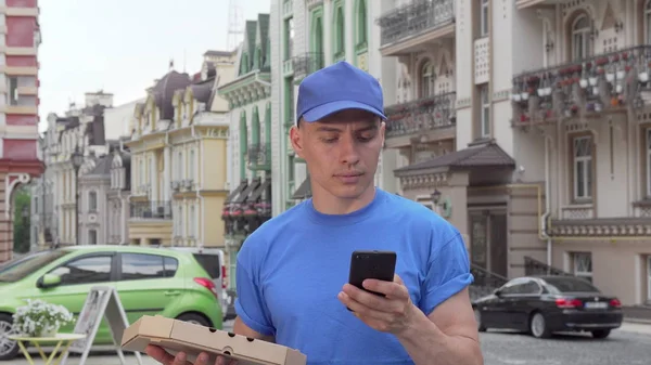 Mensageiro masculino entregando pizza na cidade chamando é cliente no telefone — Fotografia de Stock