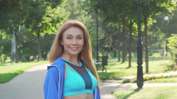 Bonita esportista feliz sorrindo para a câmera enquanto corre no parque — Fotografia de Stock