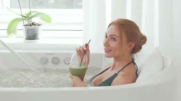 Encantadora mujer bebiendo batido de desintoxicación sentada en el baño de hidromasaje de la piscina —  Fotos de Stock