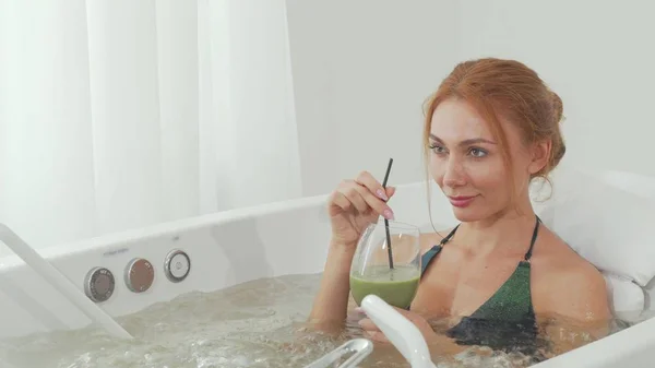 Colpo scorrevole di una bella donna sorseggiando delizioso frullato nella vasca idromassaggio — Foto Stock