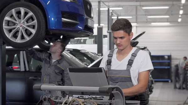 Joven mecánico de coches utilizando el ordenador portátil en el garaje — Foto de Stock