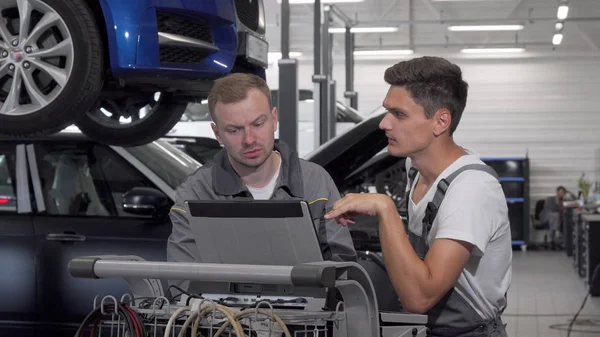 Dos mecánicos de automóviles hablando en el garaje usando el ordenador portátil en el diagnóstico de automóviles — Foto de Stock