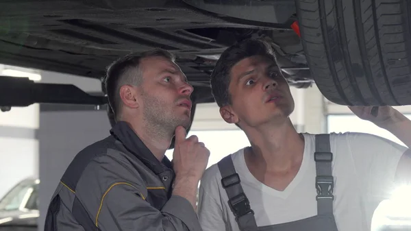 Two auto mechanics checking suspension of a lifted car at the garage — Stock Photo, Image