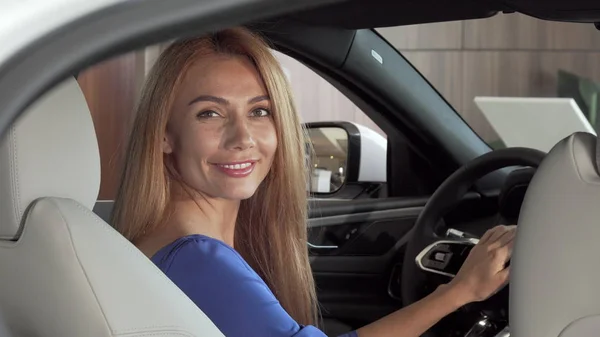 Preciosa mujer feliz sentado en un coche nuevo y caro sonriendo a la cámara — Foto de Stock