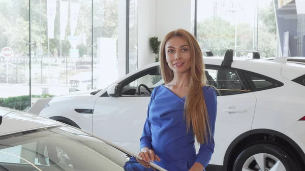 Feliz cliente femenino sonriendo a la cámara mientras elige un coche nuevo para comprar — Foto de Stock