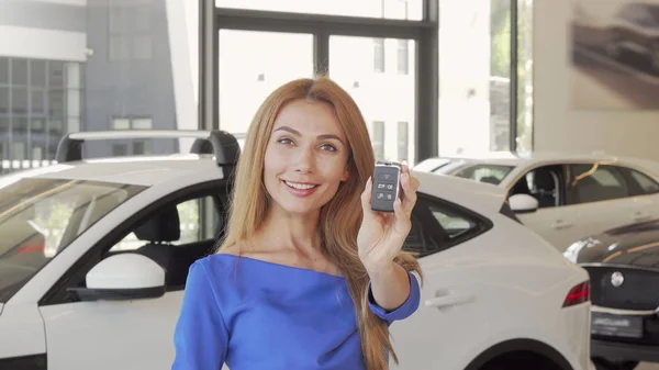 Happy female driver showing car key to the camera after buying new auto