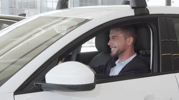 Feliz hombre guapo examinando el interior de un coche nuevo sentado dentro — Foto de Stock