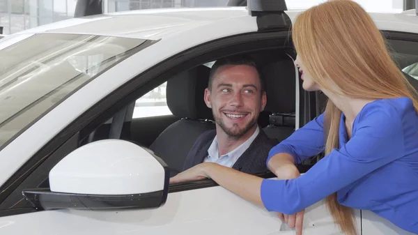 Hombre guapo hablando con su esposa mientras elige un coche nuevo en el salón de concesionarios — Foto de Stock