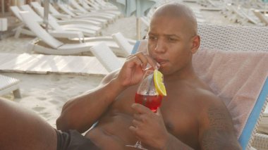 Sahilde dinlenirken kokteyl içen yakışıklı Afrikalı adam