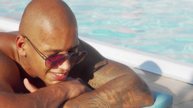 Yüzme havuzunda güneşlenmenin keyfini çıkaran mutlu bir Afrikalı adamın sürgülü fotoğrafı
