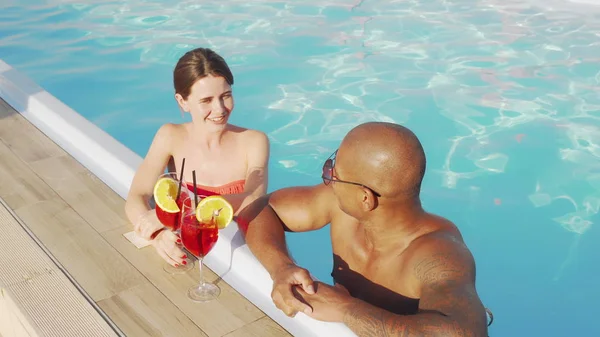 Feliz pareja multiétnica tintineo vasos en la piscina —  Fotos de Stock