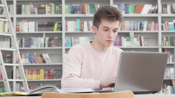 Joven estudiante masculino trabajando en su portátil en la biblioteca de la universidad — Vídeo de stock