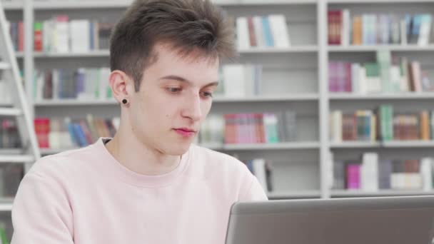 Recorte de un joven estudiante sonriendo a la cámara en la biblioteca — Vídeo de stock