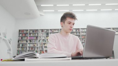 Kütüphanede laptop kullanan bir erkek öğrencinin düşük açılı görüntüsü.